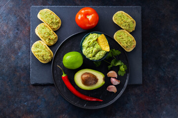 Guacamole sauce, nachos chips and ingredients on a dark background. Mexican guacamole sauce with avocado, ingredients and corn nachos. Copy space. Top view