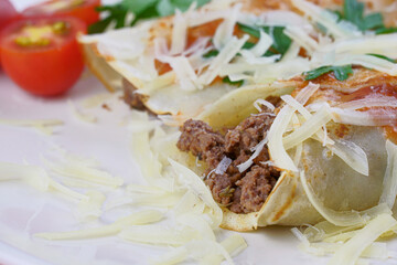 Pancakes with meat, in tomato sauce and cheese, with cilantro and grated cheese on top, and some cherry tomatoes on the plate.
