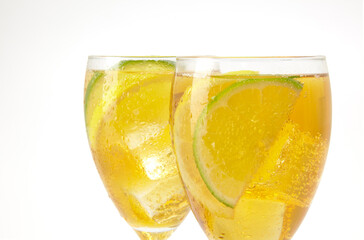 Two stemmed glasses with ice tea and lemon and lime slices on white