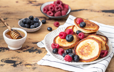 Tasty pancakes with raspberries, blueberries and honey on a plate.
