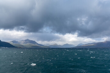 rugged and wild coastline with mountains and stormy seas with whitecaps under and expressive cloudy sky