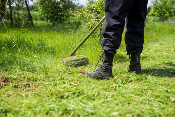 A man mows the grass with a gasoline trimmer. Close-up with selective focus.