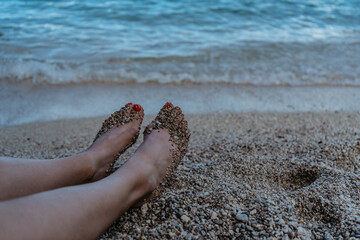 Happy woman with red nails relaxing on beach,enjoying sunny summer day,waves and turquoise sea water,feet are covered by pebbles.Travel concept banner.Relax beach vacation luxury copy space