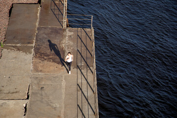 Beautiful top view of a running woman lit by the sun leaving a shadow. Running training in the evening on the embankment. Sports in the city.