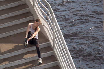 After jogging, a young woman sits down on the steps and straightens her sneakers. Beautiful background.