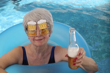 Senior woman drinking beer in swimming pool