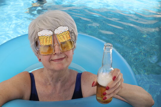 Senior woman drinking beer in swimming pool
