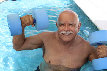 Senior man holding dumbbells in swimming pool - obrazy, fototapety, plakaty