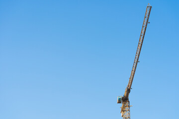 Fototapeta na wymiar High-rise crane on the Construction site with blue sky on the background