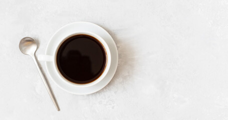 Cup of black coffee on a white concrete background. Coffee cup and silver spoon. Copy space, top view.