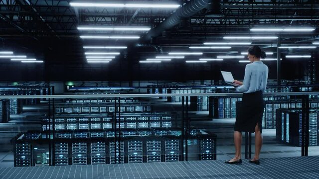 Data Center Engineer Using Laptop Computer. Server Farm Cloud Computing Specialist Facility with Multiethnic Female System Administrator Working with Data Protection Network for Cyber Security.
