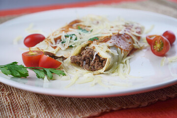 Pancakes with meat, in tomato sauce and cheese, with cilantro and grated cheese on top, and some cherry tomatoes on the plate.