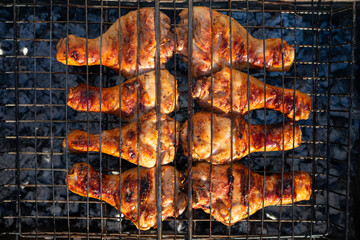 Grilled chicken meat, chicken legs on grill grid. Barbecue chicken fried on charcoal fire, top view