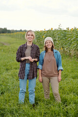 Two cheerful female farmers in workwear looking at you with smiles at farm