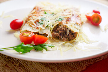 Pancakes with meat, in tomato sauce and cheese, with cilantro and grated cheese on top, and some cherry tomatoes on the plate.