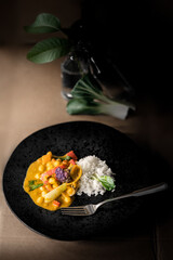 Vegetarisches Thai Curry mit Reis auf schwarzem Teller in Stimmungsvollem Licht