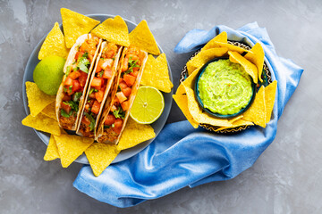 Tacos and tortilla chips on a gray background. Mexican taco, nacho chips and guacamole sauce on a...