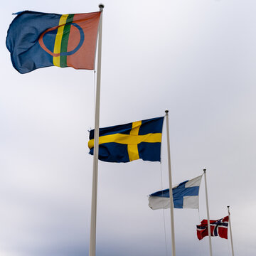 view of the flags of the Sami Nation as well as Finland and Norway and Sweden under a white overcast sky