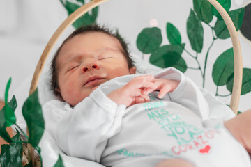 Beautiful newborn baby (4 days old), sleeping in bamboo fiber basket and surrounded by green leaves.