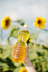 Plastic bottle with fresh sunflower oil against plants with large yellow flowers