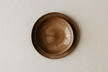 Two brown ceramic plate on beige background. Textured, grainy ceramic plate. Flat lay, top view. Minimal concept.