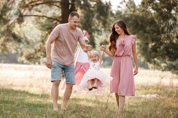 Naklejka na ściany i meble Portrait of happy family. Mom, dad and daughter walk in the park in nature. Young family spending time together on vacation, outdoors. The concept of summer holiday. Mother's, father's, baby's day
