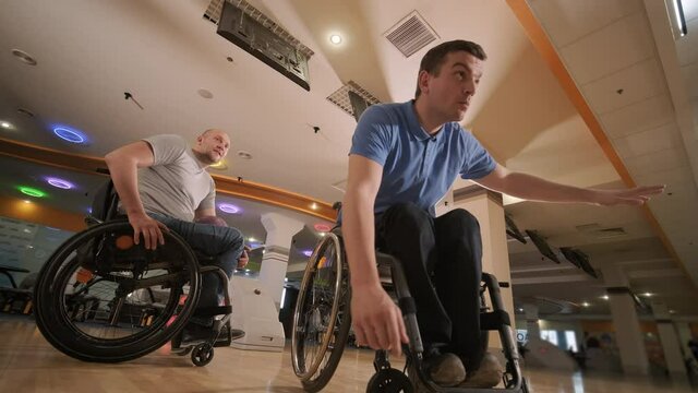 Two young disabled men in wheelchairs playing bowling in the club