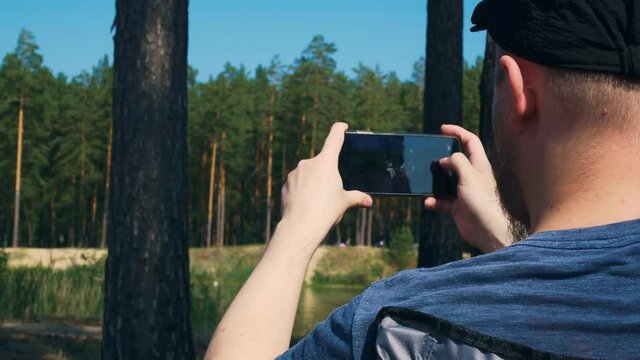 A man on a summer vacation in the forest shoots a video of nature and a lake with a forest on a smartphone. Camping in a national park for a family vacation.