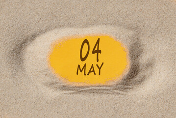 May 4. 4th day of the month, calendar date. Hole in sand. Yellow background is visible through...