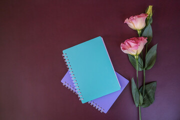 Green or purple notebook and a sprig of pink flower against a dark purple background. Flat lay, top view, copy space
