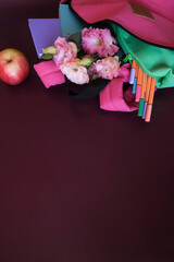 Backpack with colorful school supplies on a dark purple background. Back to school. Flat lay, top view, copy space
