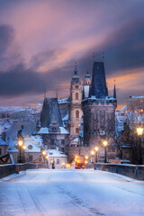 View of the lesser town bridge tower on the Charles bridge with a Saint Nicolas church in the background  in winter with dramatic sky sunrise. Lantern illumination. Snow. Statue. Sunrise. Prague.