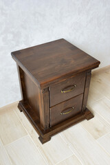 Decorative brown wooden bedside table for two drawers near the wall.
