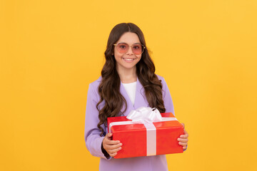 trendy cheerful kid in sunglasses and suit hold gift box on yellow background, shopping