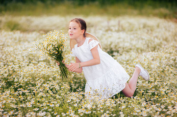 Fototapeta na wymiar Cute funny girl in a white dress with a bouquet of daisies in a field of daisies.