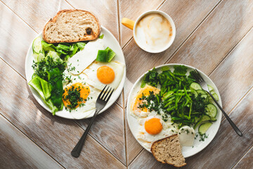 Breakfast fried eggs with green vegetables and coffee on a wooden table background, top view