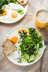 Fried eggs, bread and green vegetables for breakfast served with cup of coffee on wooden table