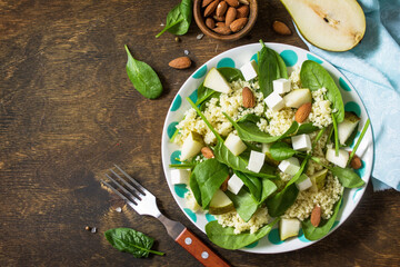 Autumn fruit salad. Couscous salad with pear, spinach, feta cheese and vinaigrette sauce on a wooden rustic table. Top view flat lay background. Copy space.