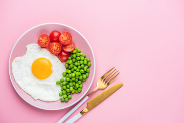 Breakfast eggs with green peas and tomatoes on a pink plate, pink background, top view with copy space. Healthy breakfast meal