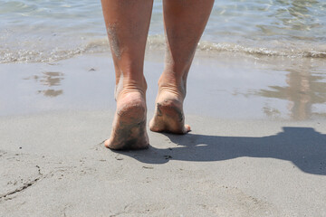 Female feet walk on the beach towards seawater on a summer day. Close up, copy space