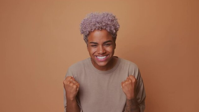 Excited cheerful dark skinned woman clenches fists exclaims with victory willing to win, gets first prize, roots for team, dressed in casual wear, shouts yeah isolated on brown wall. Grab this chance
