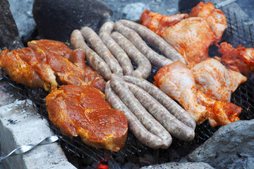 marinated raw chicken legs and wings lie next to grilled sausages . side view. food prepared in nature