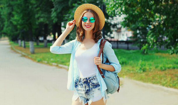 Summer portrait of beautiful smiling young woman wearing a straw hat and backpack in the city park