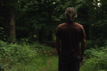Fototapeta premium Blonde man in brown t-shirt on a forest path in summer. Rear vie