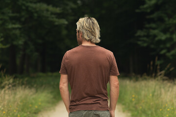 Blonde man in a brown t-shirt on a sandy path in a forest in sum