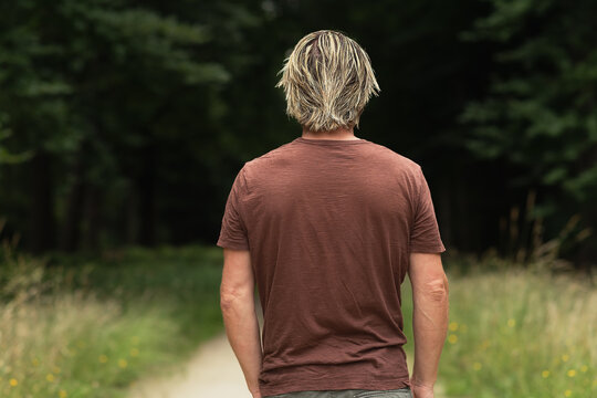 Blonde man in a brown t-shirt on a sandy path in a forest in sum