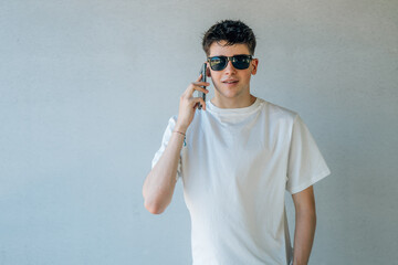 Naklejka premium teen boy with mobile phone and sunglasses isolated on wall background