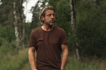 Blonde man with a stubble beard in a brown t-shirt on a forest p