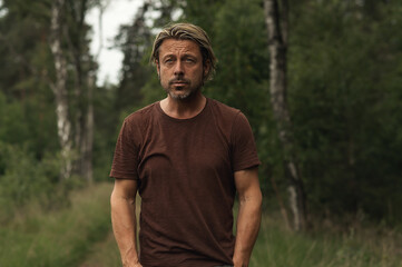 Naklejka na ściany i meble Blonde man with a stubble beard in a brown t-shirt on a forest p