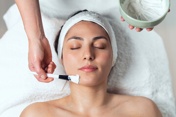 Cosmetologist applying the alginates facial mask to woman while lying on a stretcher in the spa center.